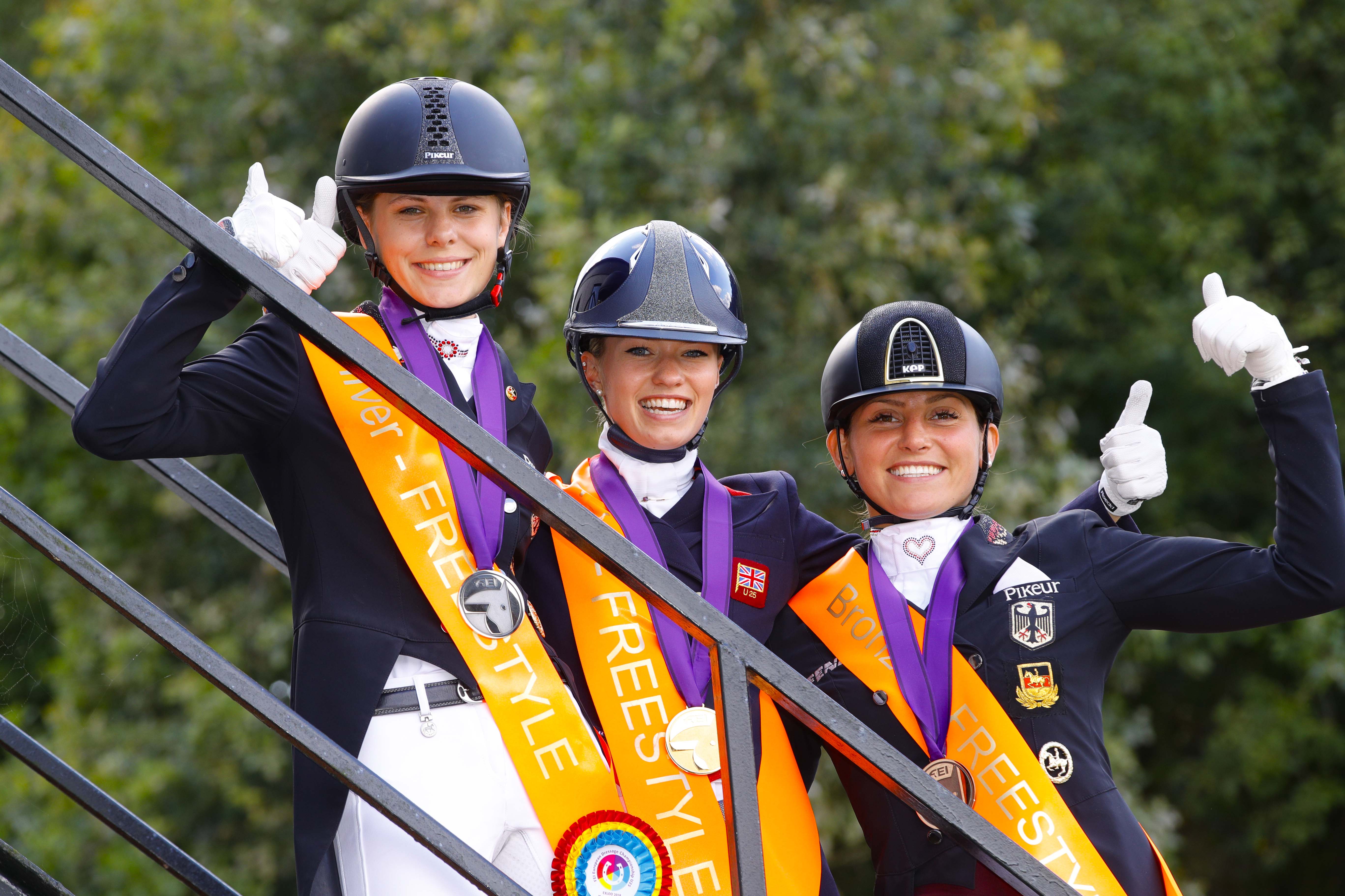 It’s a big thumbs up from Jil-Marielle Becks GER (silver), Charlotte Fry GBR (gold) and Lisa Maria Klossinger GER (bronze) after stepping off the Freestyle podium at the FEI European Dressage Championships U25 2018 in Exloo, The Netherlands today. FEI/Leanjo de Koster, DigiShots