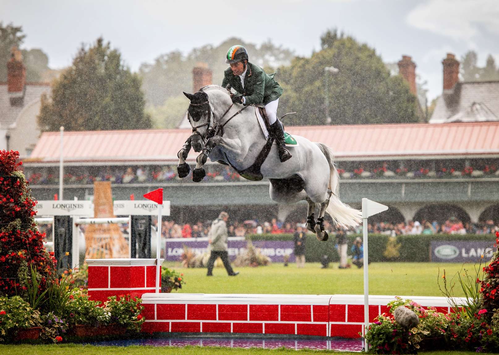 Cian O'Connor and a grey horse tackling a showjumping water jump in arena.