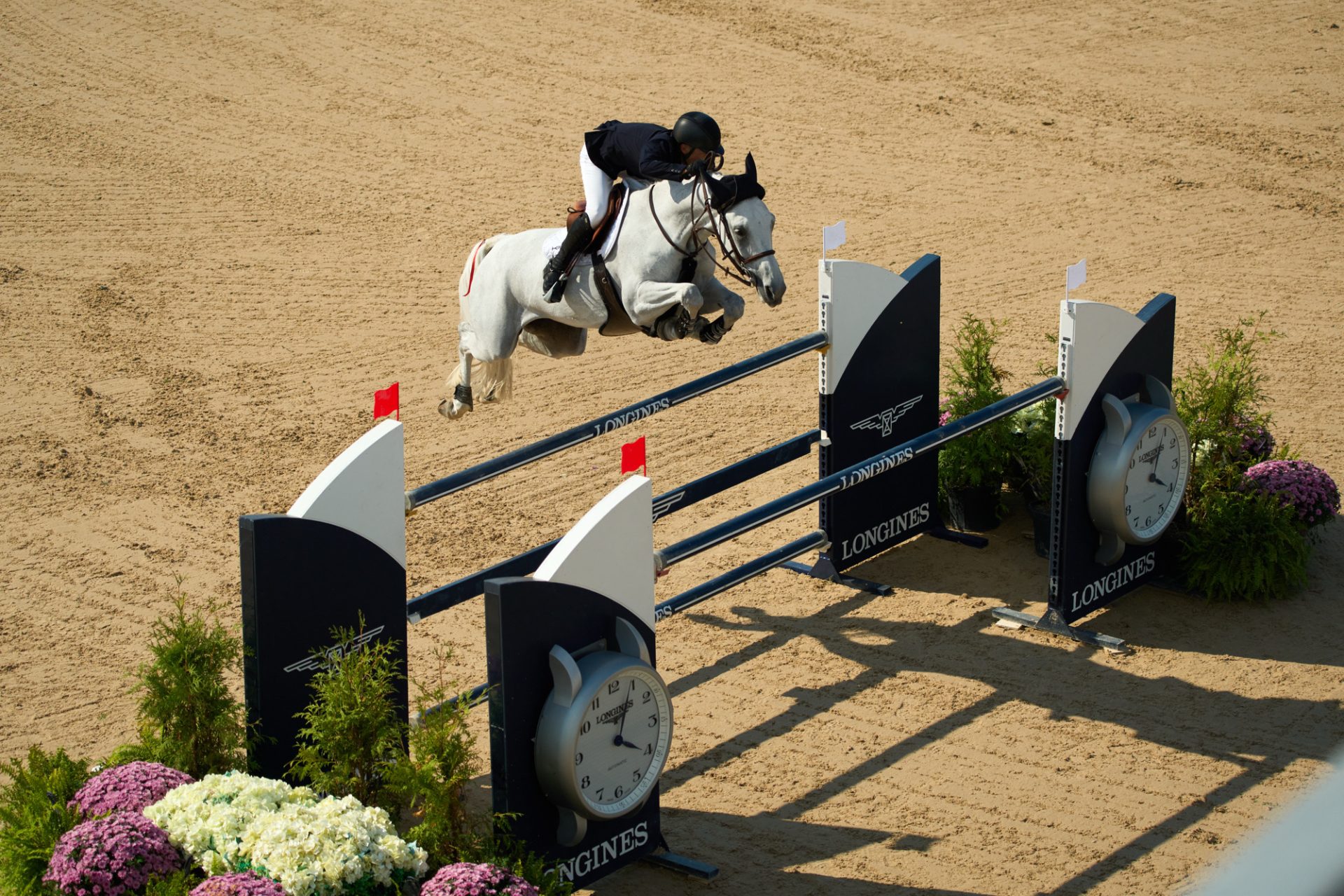 an aerial view of a grey horse and riding jumping a large longines fence